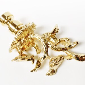 May include: Gold-toned metal lamp finial with a detailed design of a tree branch with birds perched on it.