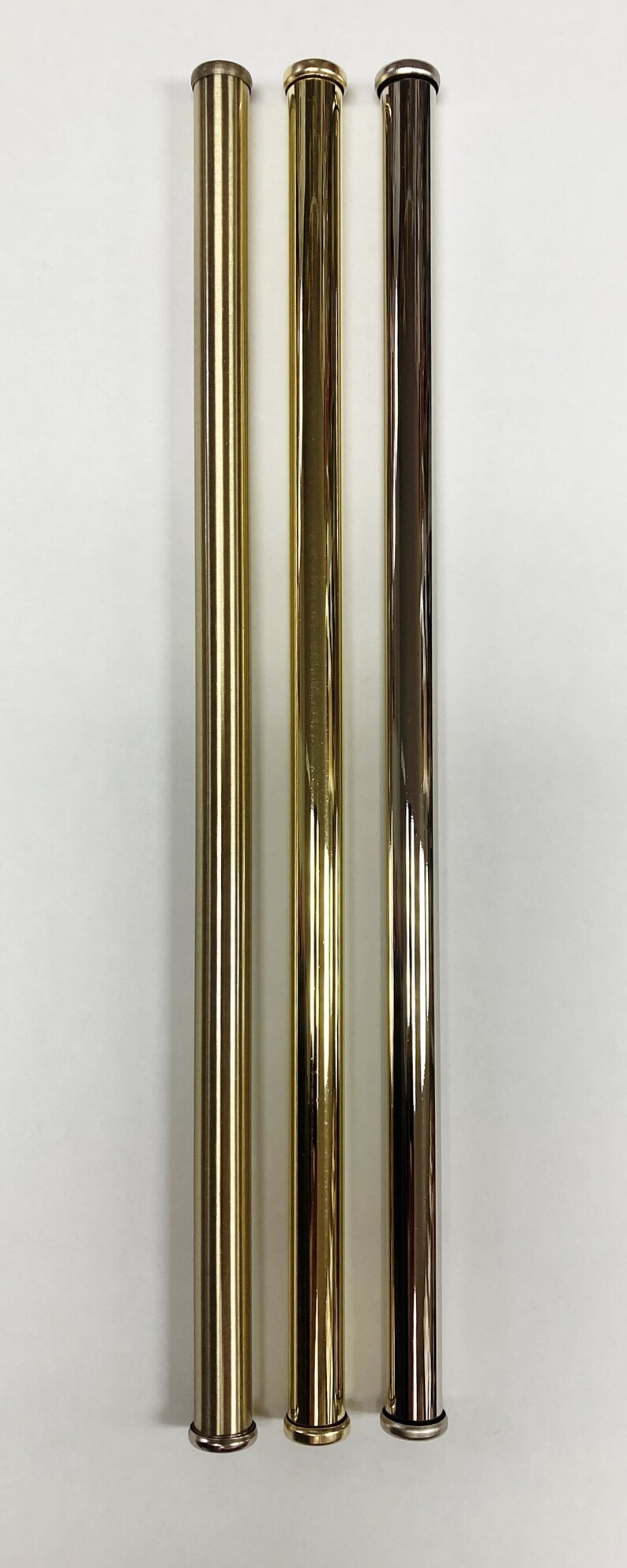 May include: Three metallic tubes in varying shades of gold and bronze. The tubes are cylindrical, with a consistent diameter and a rounded cap on each end. The surfaces reflect light, creating highlights and shadows.