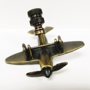 Puede incluir: Un tap&oacute;n de botella de bronce con forma de avi&oacute;n, con una h&eacute;lice y un dise&ntilde;o detallado. El tap&oacute;n tiene una parte superior negra con un dise&ntilde;o roscado.