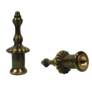 May include: Two antique gold metal finials with a decorative fluted design. The finial on the left has a round base, while the finial on the right has a threaded end.