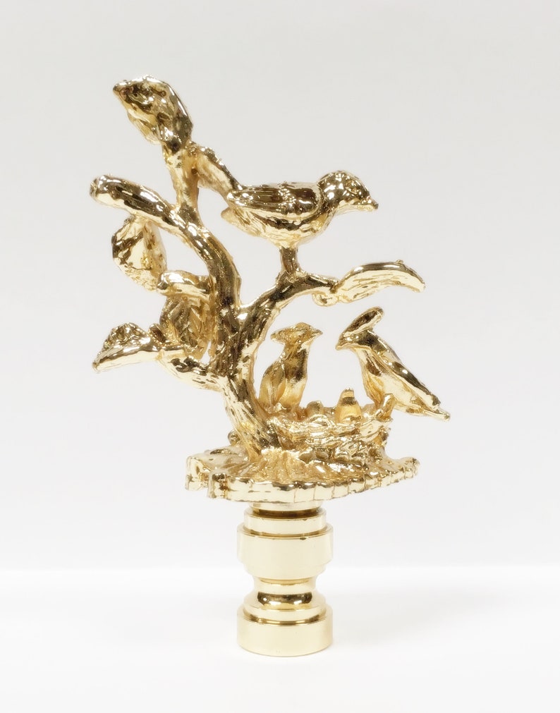 May include: Gold metal lamp finial with a detailed design of birds in a nest on a tree branch.