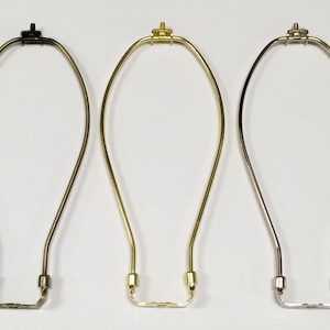 May include: Three lamp harp finials in different finishes: black, brass, and nickel. Each harp is made of metal and has a simple, elegant design.