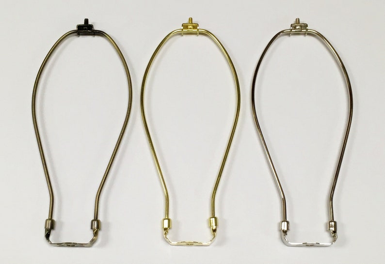May include: Three lamp harp finials in different finishes: black, brass, and nickel. Each harp is made of metal and has a simple, elegant design.