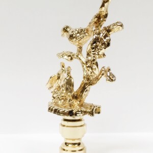 May include: Gold lamp finial with a tree branch design and three birds perched on the branches.