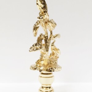 May include: Gold metal lamp finial with a detailed design of a tree with leaves and branches.