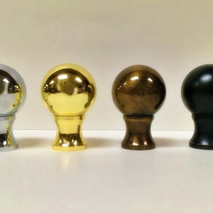 May include: Four finials in different finishes: chrome, gold, bronze, and black. Each finial has a round ball shape on top of a short, cylindrical base.