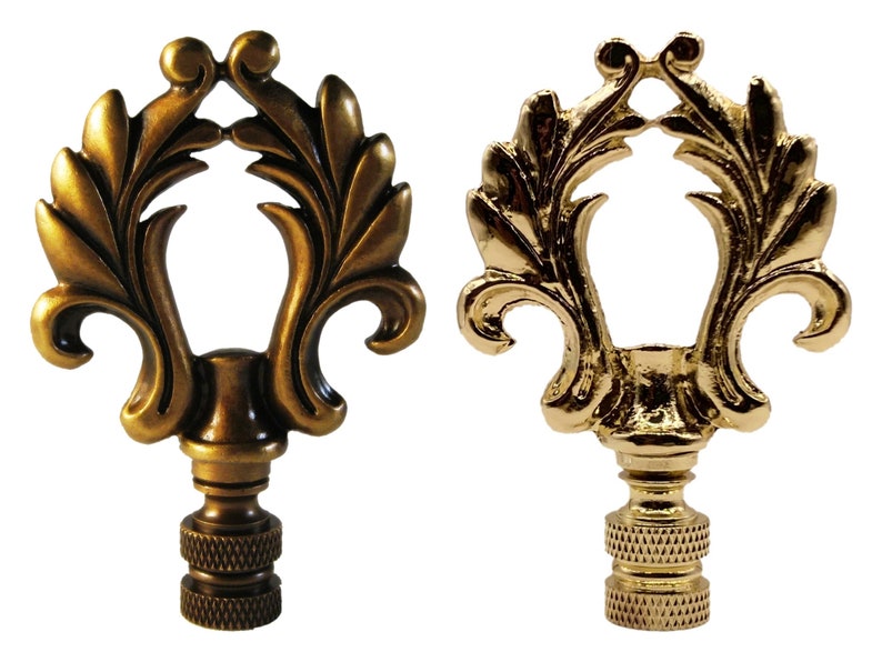 May include: Two ornate lamp finials with a gold finish. The finial on the left has a more antique brass finish, while the finial on the right has a polished gold finish. Both finials feature a decorative leaf design.