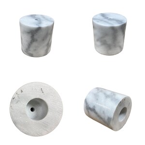 K&ouml;nnte beinhalten: Vier wei&szlig;e Marmorzylinder-Kerzenhalter mit einem Loch in der Mitte. Die Halter werden aus verschiedenen Blickwinkeln gezeigt.