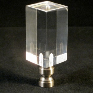 May include: A clear acrylic lamp finial with a square shape and a brushed nickel base.