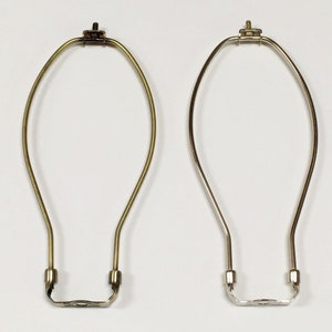 May include: Two lampshade harp rings, one gold and one silver, are shown against a white background. The rings are made of metal and have a simple, classic design.