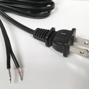 May include: A black electrical cord with a standard two-prong plug. The cord is stripped at the end, showing the bare copper wires.