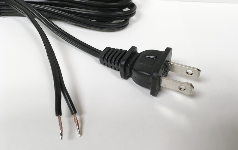 May include: A black electrical cord with a standard two-prong plug. The cord is stripped at the end, showing the bare copper wires.