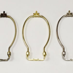 May include: Three lamp harp rings in different finishes: brass, gold, and silver. Each ring is made of metal and has a simple, elegant design.