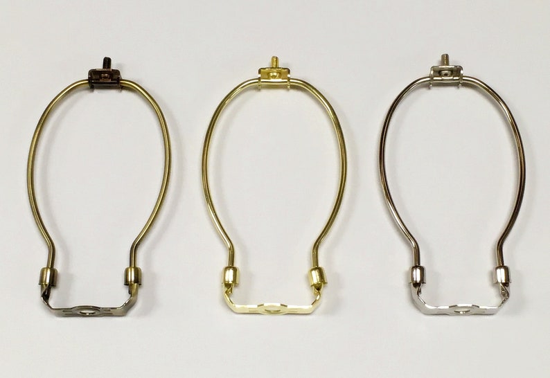 May include: Three lamp harp rings in different finishes: brass, gold, and silver. Each ring is made of metal and has a simple, elegant design.