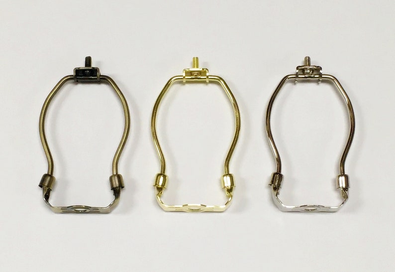 May include: Three lamp harp sockets in different finishes: black, gold, and silver. Each harp socket is made of metal and has a curved shape.