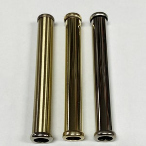 May include: Three metallic tubes in gold, brass, and silver tones are arranged vertically against a white background. Each tube has a rounded base and a cylindrical body. The tubes are of similar length and diameter.