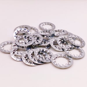 May include: A pile of silver-colored metal washers with a serrated edge. The washers are arranged in a random pattern.