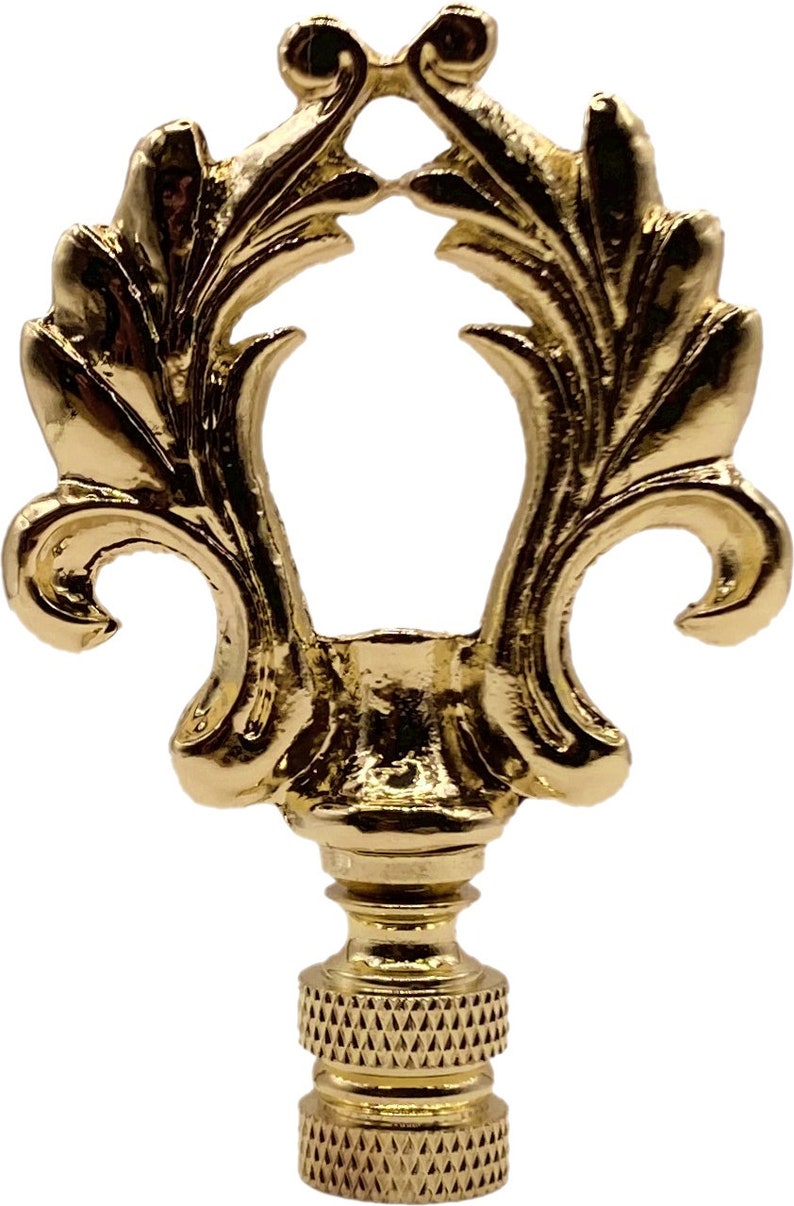 May include: Gold metal lamp finial with a decorative, ornate design. The finial has a leaf-like pattern and a round opening in the center.