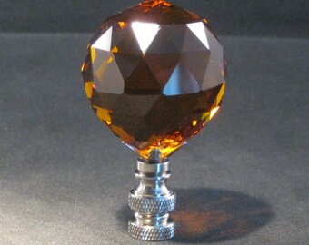 May include: A faceted amber glass finial with a silver metal base. The finial is a sphere with many facets and the base is a threaded cylinder.