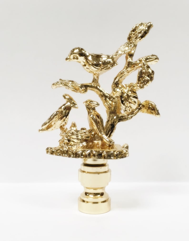 May include: Gold metal lamp finial with a detailed design of birds in a tree. The finial is a decorative piece for a lamp.
