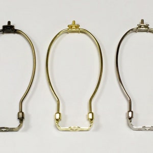 May include: Three lamp harp rings in different finishes: black, gold, and silver. Each ring is made of metal and has a simple, elegant design.