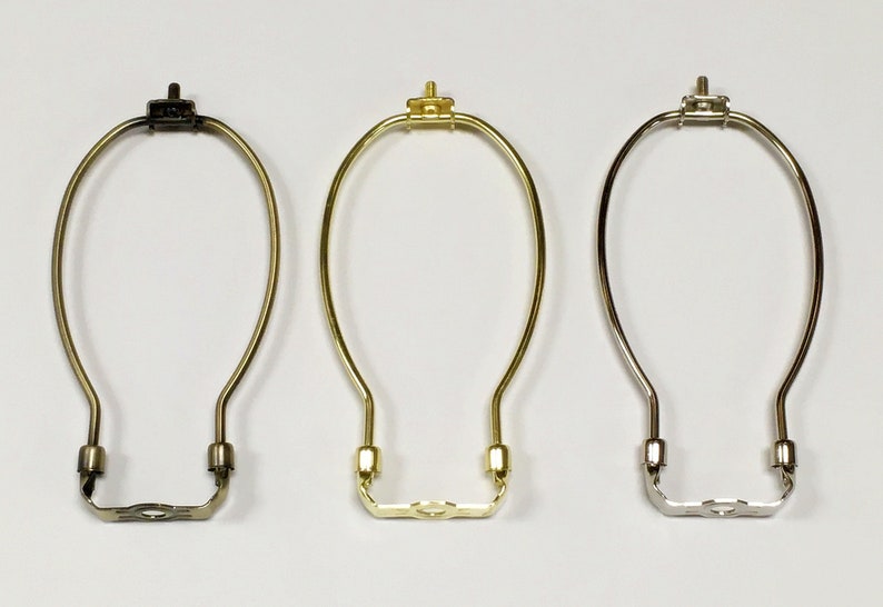 May include: Three lamp harp rings in different finishes: black, gold, and silver. Each ring is made of metal and has a simple, elegant design.