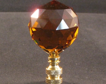 May include: A gold-toned lamp finial with a faceted amber glass orb on top. The orb is a geometric shape with many facets.