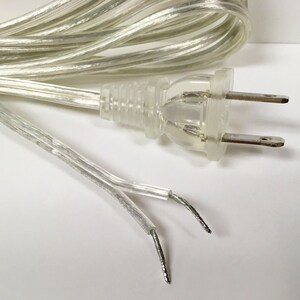 May include: A clear, transparent electrical cord with a two-prong plug. The cord is coiled and the ends are visible.