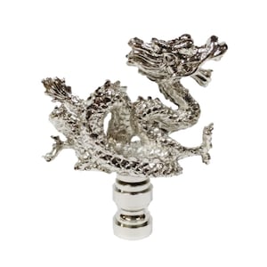 May include: A silver dragon lamp finial with a detailed design. The dragon is curled up with its head raised and its mouth open. The finial is attached to a round base.
