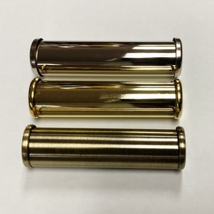 May include: Three metallic, cylindrical objects in varying shades of gold and bronze. The top one is a shiny silver-gold, the middle is a bright gold, and the bottom is a darker bronze. Each has a rounded end.