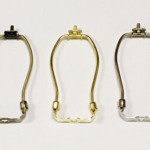 May include: Three lamp harp adapters in different finishes: black, brass, and nickel. Each harp adapter has a screw-on top and a U-shaped bottom with a center hole.