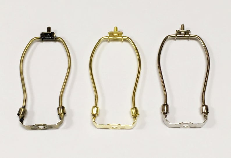 May include: Three lamp harp adapters in different finishes: black, brass, and nickel. Each harp adapter has a screw-on top and a U-shaped bottom with a center hole.