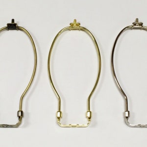 May include: Three lamp harp rings in different finishes: black, gold, and silver. The rings are made of metal and have a simple, elegant design.