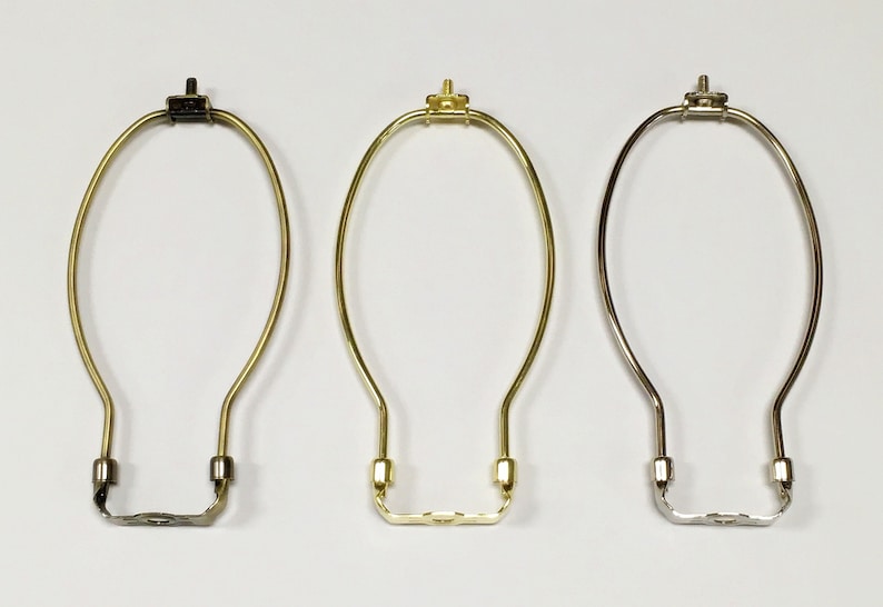 May include: Three lamp harp rings in different finishes: black, gold, and silver. The rings are made of metal and have a simple, elegant design.