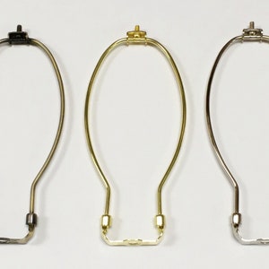 May include: Three lampshade harp rings in different finishes: black, gold, and silver. Each harp ring is made of metal and has a simple oval shape.
