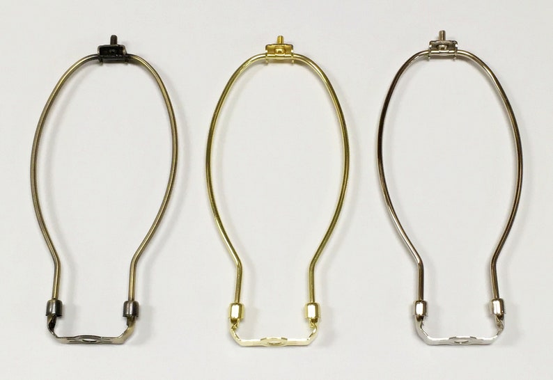 May include: Three lampshade harp rings in different finishes: black, gold, and silver. Each harp ring is made of metal and has a simple oval shape.