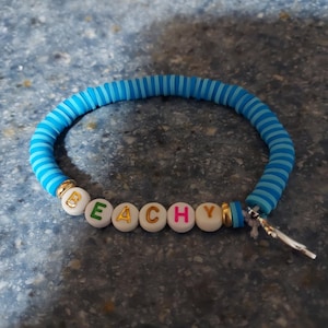 Pulsera elástica azul con diseño playero de delfines. Tiene cordón elástico blanco.