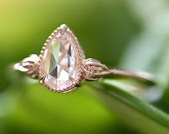 May include: A pear-shaped diamond engagement ring set in rose gold with delicate floral details on the band.