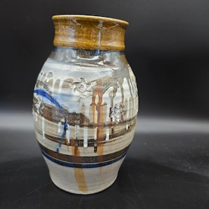 May include: A ceramic vase with a wide, rounded body and a narrow neck. The surface features a light gray base with horizontal brown and blue stripes, accented by white and brown glaze drips and small, embossed flower-like patterns throughout.
