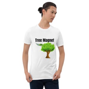 Könnte beinhalten: Weißes T-Shirt mit dem Text "Tree Magnet" und einer Grafik eines grünen Baumes mit braunem Stamm. Über dem Baum ist eine grüne Scheibe abgebildet. Das T-Shirt ist ein lässiger Unisex-Stil, geeignet für den Alltag.