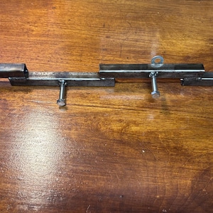 May include: A metal gate latch, constructed from welded steel tubing. The latch features a series of rectangular bars connected with bolts and eyelets. The metal has a raw, unfinished appearance, with visible weld marks.