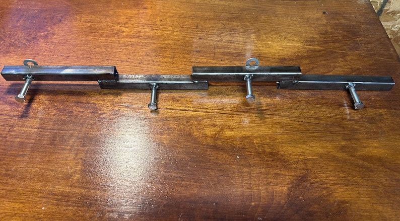 May include: A metal gate latch, constructed from welded steel tubing. The latch features a series of rectangular bars connected with bolts and eyelets. The metal has a raw, unfinished appearance, with visible weld marks.