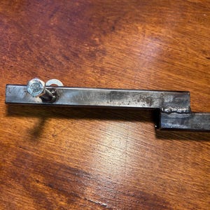 May include: A metal bracket with a bolt and washer attached. The bracket has the letters "WWE" stamped on it. The bracket is made of steel and has a welded joint. The bracket is on a wooden surface.