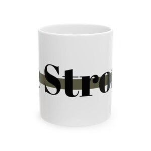 May include: White ceramic mug with the word "Strong" in black, centered horizontally. The word is overlaid on a horizontal olive green stripe. The mug is cylindrical and has a simple, clean design.
