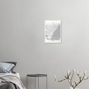 May include: A framed monochrome map print of Barcelona, Spain. The map depicts the city's layout, including roads and the coastline. The word "Barcelona" is printed at the bottom of the map.