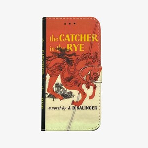 Pu&ograve; includere: Una custodia per telefono rossa e bianca con un design di copertina di libro vintage. La copertina presenta un cavallo rosso e il testo "the CATCHER in the RYE a novel by J.D. SALINGER".