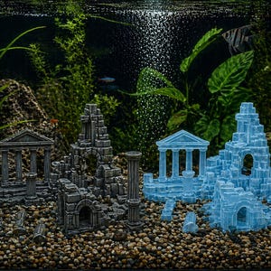 May include: Aquarium decorations featuring miniature ancient ruins in shades of gray and blue. The scene includes columns, archways, and building fragments, creating an underwater landscape. The background has live plants and fish.