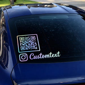 May include: A holographic vinyl decal applied to a dark blue car rear window. The decal features a square QR code and the Instagram logo followed by the text Customtext in a cursive font, displaying a multi-colored iridescent finish.
