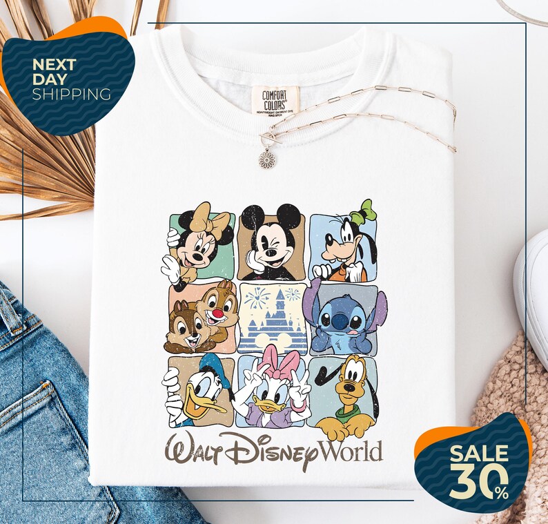 A white t-shirt with a graphic design featuring various Disney characters, including Minnie Mouse, Mickey Mouse, Goofy, Donald Duck, and Pluto, arranged in a grid pattern.