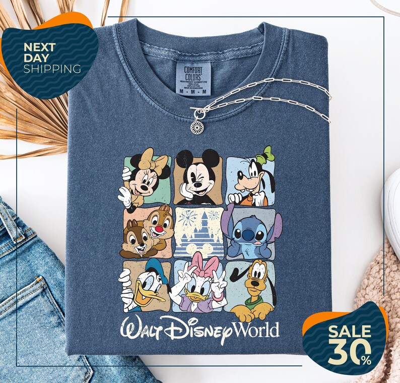 A t-shirt with a graphic of Disney characters, including Minnie Mouse, Mickey Mouse, Goofy, Donald Duck, and Pluto, arranged in a square pattern. The t-shirt is displayed on a white background, and there are jeans and a sweater visible in the background.